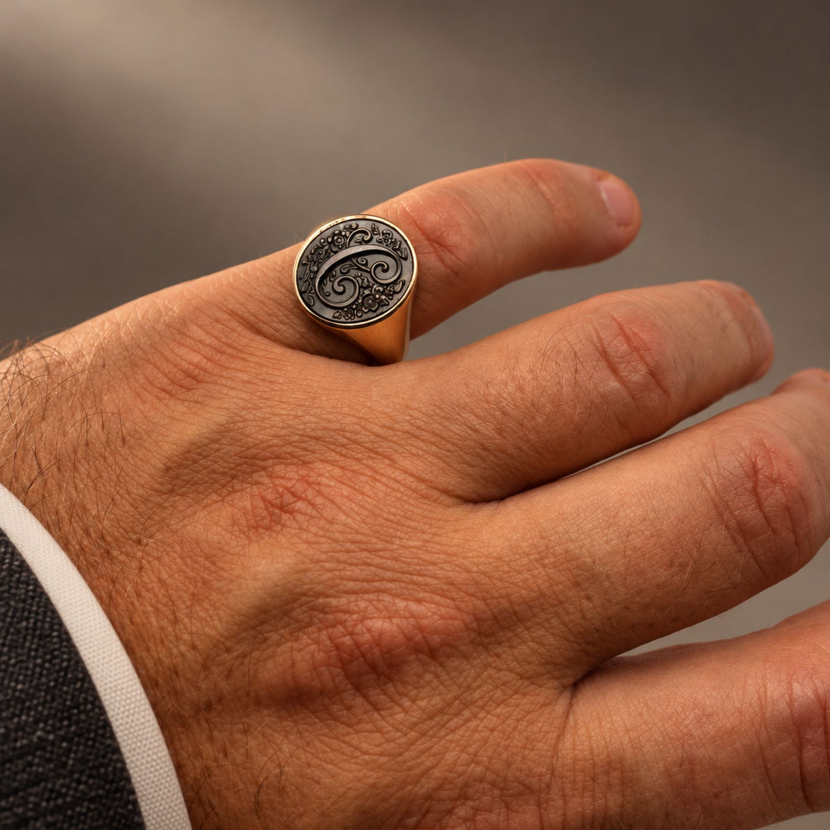 Mano maschile che indossa un anello a sigillo in bronzo con l'iniziale C incisa su madreperla grigia - Man's hand wearing a bronze signet ring with a carved initial C on grey mother of pearl